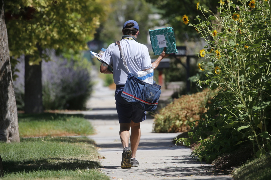 FILE - In this Aug. 17, 2020, file photo, a United States Postal Service carrier delivers mail to homes in Salt Lake City. A Center for Public Integrity investigation finds that the U.S. Postal Service regularly cheats mail carriers out of their pay. Arbitrators and federal investigators have found managers at hundreds of post offices around the country have illegally underpaid hourly workers for years.