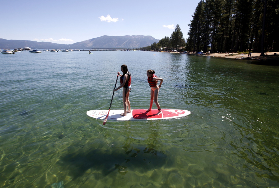 FILE - In this Aug. 20, 2019, file photo, Freya Mayo, left, and her sister Evie, of London, try out a paddle board on Lake Tahoe near South Lake Tahoe, Calif. With wildfire no longer threatening Lake Tahoe, residents, tourists and scientists drawn to its clean alpine air, clear blue waters and fragrant pine trees now wonder about the long-term effects that will remain after wildfire season ends.