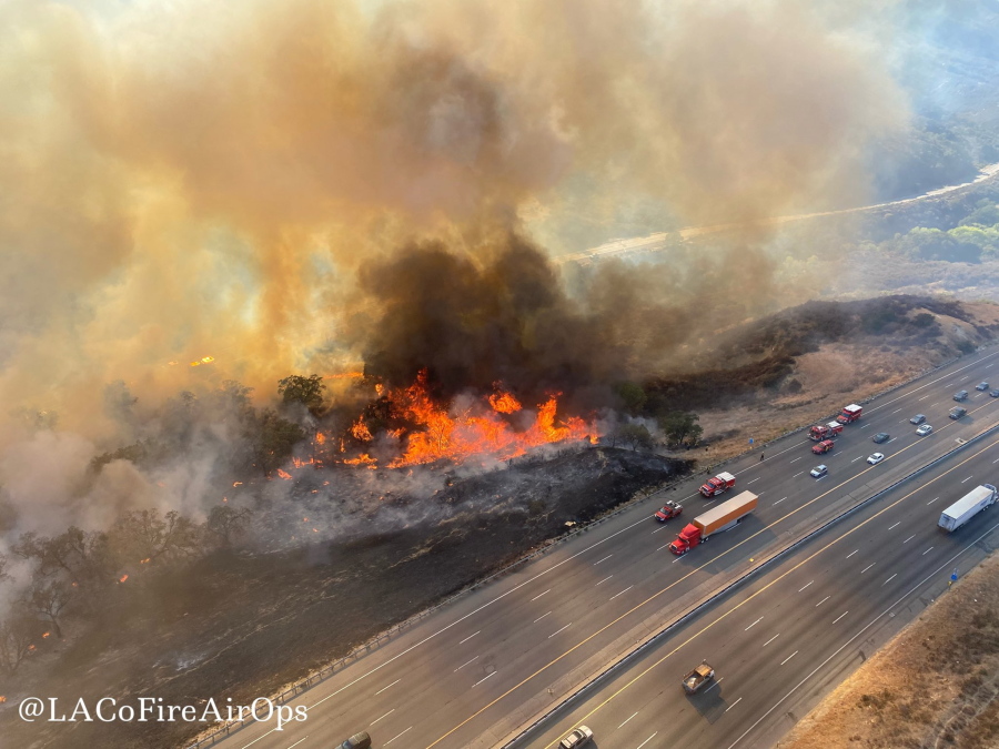 In this aerial photo released by the Los Angeles County Fire Department Air Operations traffic passes the Route fire, a brush wildfire off Interstate 5 north of Castaic, Calif., on Saturday, Sept. 11, 2021.