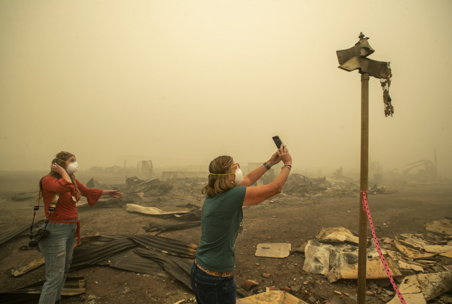 Kelly Tan, 59, left, looks on as her sister, Tiffany Lozano, 44, photographs melted street signs on Main St. in Greenville, California, caused by the extreme temperature of the Dixie Fire that destroyed most of the town. Lozano is a resident of nearby Quincy and Tan is a resident of nearby Taylorsville.
