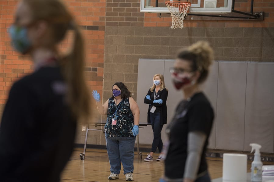 Paraeducator Darcy Wells, in a purple mask, greets a parent as they enter the gym to pick up an iPad for a child at Washington Elementary School at the onset of the pandemic in early 20202.