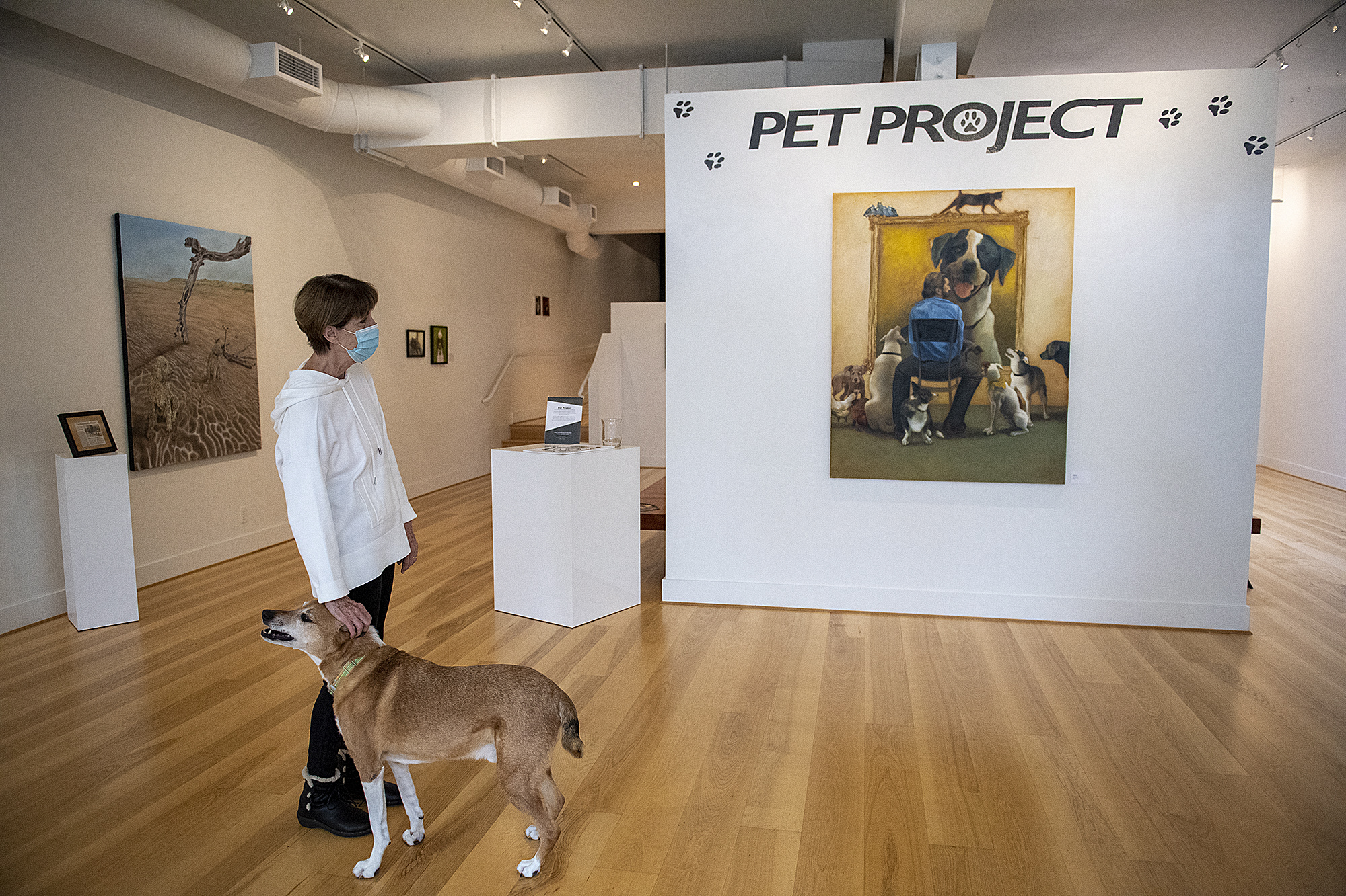 Vancouver artist Anne John joins her dog, Paddy, 10, as they look over the “Pet Project” exhibit, including her piece, “Adopted,” right, at Art at the CAVE.