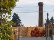 Construction workers continue building an apartment building Tuesday, Oct. 19, 2021, as the Providence Academy smokestack stands in the distance. The Vancouver City Council decided Monday to uphold a demolition permit for Providence AcademyÄôs landmark smokestack.