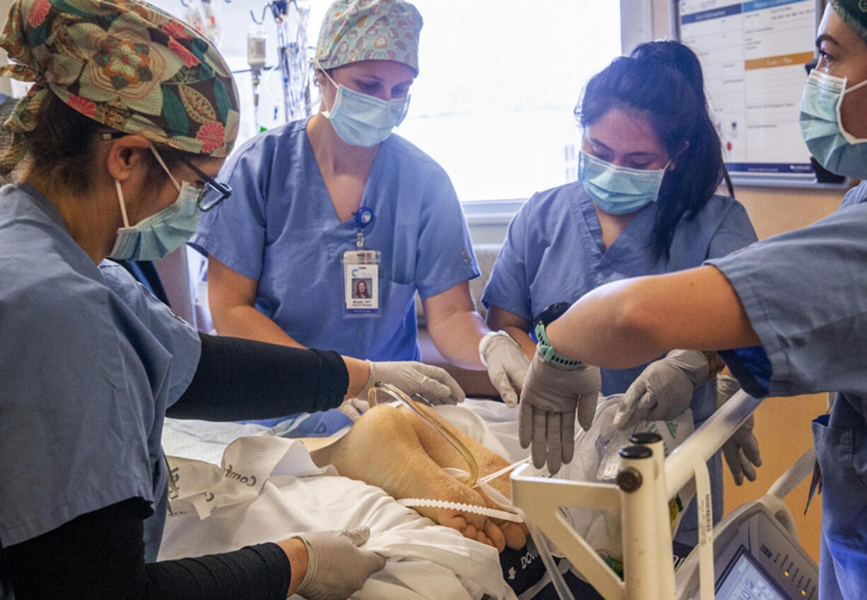 A medical team adjusts tubes and cords after turning a COVID-19 patient onto their stomach to help with breathing, inside the intensive care unit at Central Washington Hospital on Tuesday, Sept. 21, 2021. The medical team isn't wearing protective gear because the patent isn't contagious anymore.