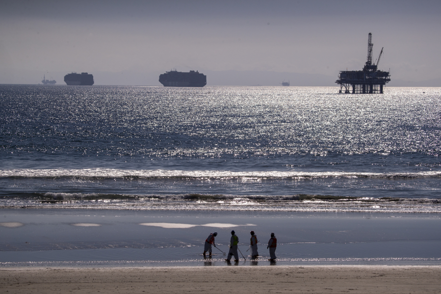 Container ships and an oil derrick line the horizon as environmental oil spill cleanup crews search the beach, cleaning up oil chucks from a major oil spill in Huntington Beach, California on Tuesday, Oct. 5, 2021. (Allen J.