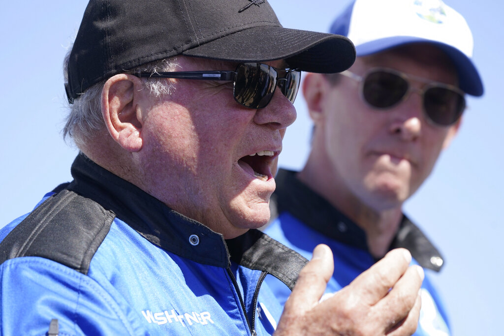 William Shatner, center, describes his flight on the Blue Origin as Glen de Vries looks on during a media availability at the spaceport near Van Horn, Texas, Wednesday, Oct. 13, 2021.  The “Star Trek” actor and three fellow passengers hurtled to an altitude of 66.5 miles (107 kilometers) over the West Texas desert in the fully automated capsule, then safely parachuted back to Earth in a flight that lasted just over 10 minutes.