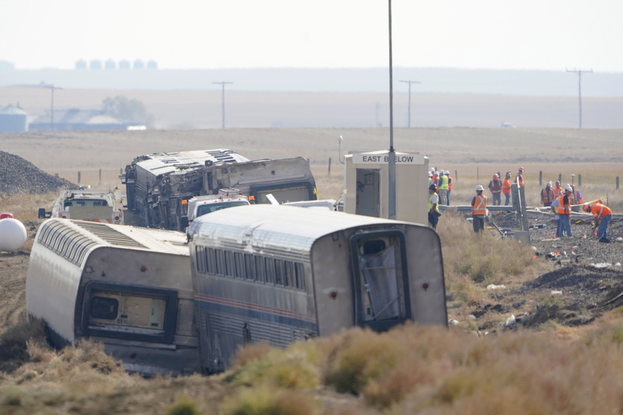FILE - In this Sept. 27, 2021, file photo, workers stand near train tracks next to overturned cars from an Amtrak train that derailed near Joplin, Mont.  A preliminary report released Tuesday, Oct. 16, 2021, on the derailment of an Amtrak train in north-central Montana last month that killed three people and injured dozens more gave no information on the cause of the accident. (AP Photo/Ted S.