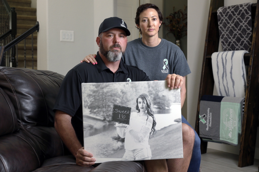 In this Oct. 12, 2021, photo, David and Wendy Mills, parents of Kailee Mills who was killed four years ago in an automobile accident when riding in the back seat without a seat belt, with a photo of their daughter at their home in Spring, Texas. The teenager was riding in the back seat of a car to a Halloween party in 2017 just a mile from her house when she unfastened her seat belt to slide next to her friend and take a selfie. Moments later, the driver veered off the road and the car flipped, ejecting her.