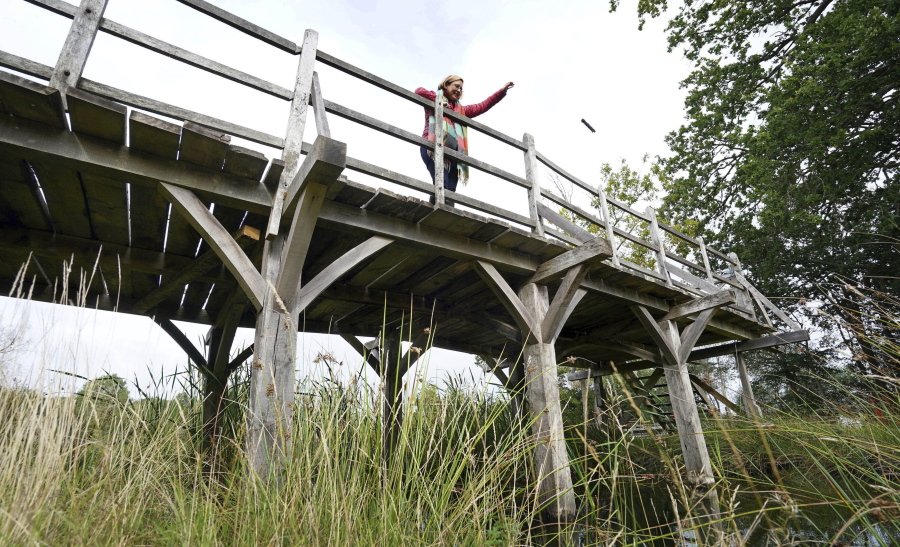 Silke Lohmann of Summers Place Auctions stands on the original Poohsticks Bridge from Ashdown Forest, featured in A.A. Milne's Winnie the Pooh books and E.H. Shepard's illustrations, near its original location in Tonbridge, Kent, England, Thursday, Sept. 30, 2021. The adventures of the honey-loving bear "Winnie the Pooh" have captivated children and their parents for nigh on 100 years. Fans now have a chance to own a central piece of Pooh's history, when a countryside bridge from the south of England goes up for auction next week. The author of the hugely popular Pooh series of books, A. A. Milne, often played with his son, Christopher Robin, at the bridge in the 1920s. The bridge became a regular setting for the adventures of Pooh and his friends in the series that launched in 1926. The auctioneers have said there's been interest from around the world, but hoped that it stays local.