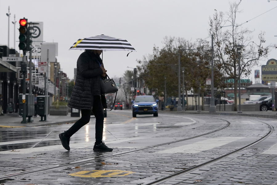 A pedestrian carries an umbrella while crossing a street at Fisherman's Wharf in San Francisco, Wednesday, Oct. 20, 2021. Showers drifted across the drought-stricken and fire-scarred landscape of Northern California on Wednesday, trailed by a series of progressively stronger storms that are expected to bring significant rain and snow into next week, forecasters said.