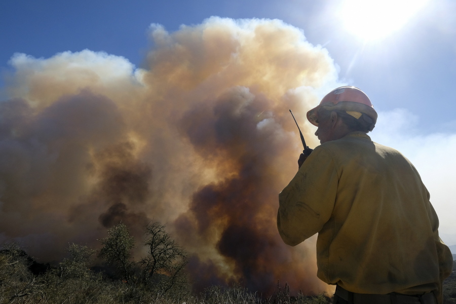 FILE - In this Oct. 13, 2021, file photo, a firefighter watches as smoke rises from a wildfire in Goleta, Calif.  Worsening climate change requires that the United States do much more to track and manage flows of migrants fleeing natural disasters. That's the finding of a multiagency study from the Biden administration. President Joe Biden ordered the assessment.  (AP Photo/Ringo H.W.
