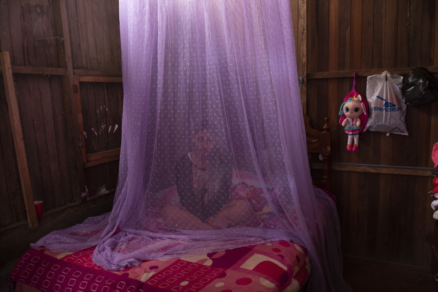 FILE - In this Tuesday, Sept. 29, 2020 file photo, Valentina Esperanza, who is recovering from dengue, sits on her bed protected by mosquito netting as she watches a television program at her home in Pucallpa, in Peru's Ucayali region. Health problems tied to climate change are all getting worse, according to two reports published in the medical journal Lancet on Wednesday, Oct. 20, 2021. The environment in some places is now more conducive to certain mosquitoes that carry malaria and dengue fever.