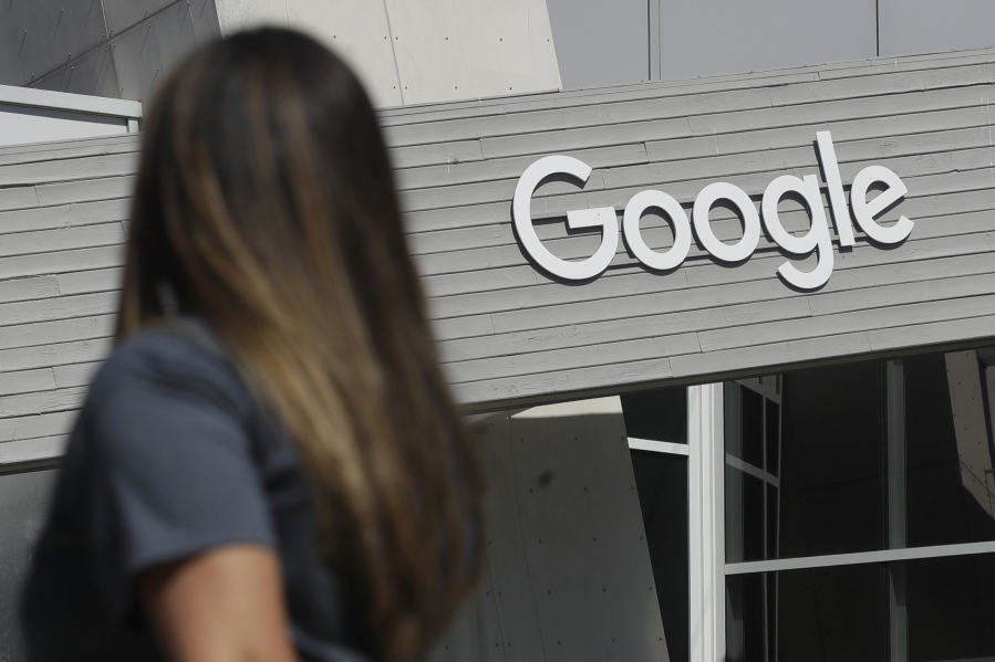 FILE - In this Sept. 24, 2019, file photo, a woman walks below a Google sign on the campus in Mountain View, Calif.  Google on Thursday, Oct. 7, 2021, will no longer allow digital ads promoting false climate change claims to appear next to the content of other publishers, hoping to deny money to those making such claims and to stop the spread of misinformation on its platform.