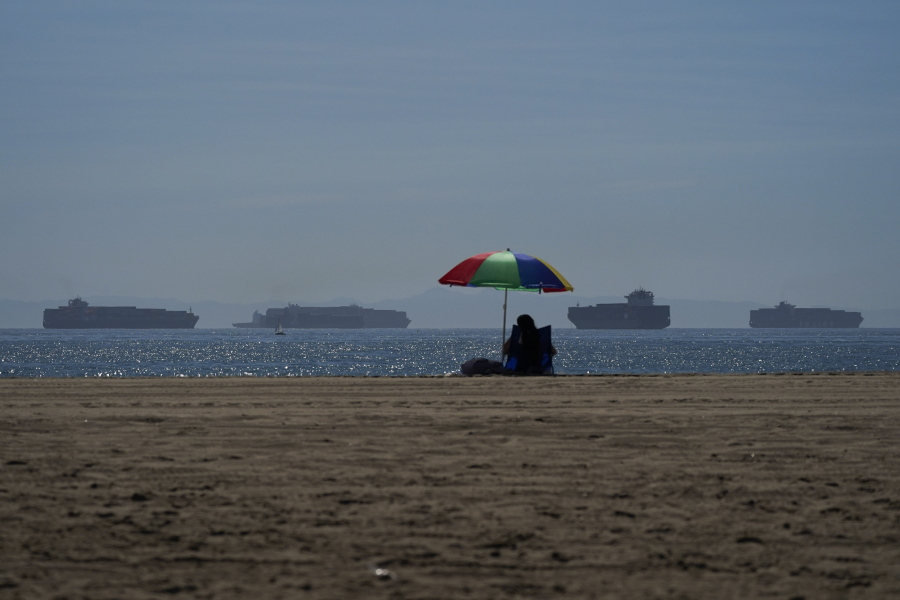 A beach goer sits on the beach in Seal Beach Calif., Friday, Oct. 1, 2021, as container ships waiting to dock at the Ports of Los Angeles and Long Beach are seen in the distance. With three months until Christmas, toy companies are racing to get their toys onto store shelves as they face a severe supply network crunch. Toy makers are feverishly trying to find containers to ship their goods while searching for new alternative routes and ports. (AP Photo/Jae C.