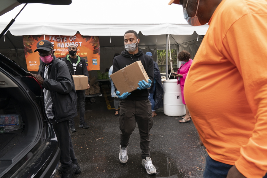 Volunteer Markel Lucas, center, takes a box of food to a patron of the food bank's car, at the Town Hall Education Arts & Recreation Campus (THEARC), Wednesday, Oct. 6, 2021, in Washington.