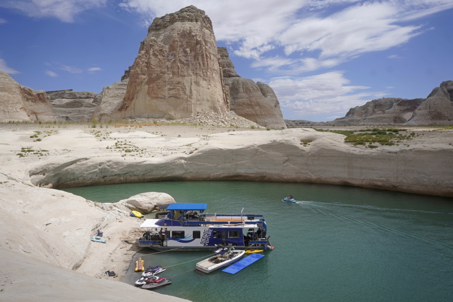 FILE - In this Friday, July 30, 2021 file photo, a houseboat rests in a cove at Lake Powell near Page, Ariz. This summer, the water levels hit a historic low amid a climate change-fueled megadrought engulfing the U.S. West.  Severe drought across the West drained reservoirs this year, slashing hydropower production and further stressing the region's power grids. And as extreme weather becomes more common with climate change, grid operators are adapting to swings in hydropower generation.