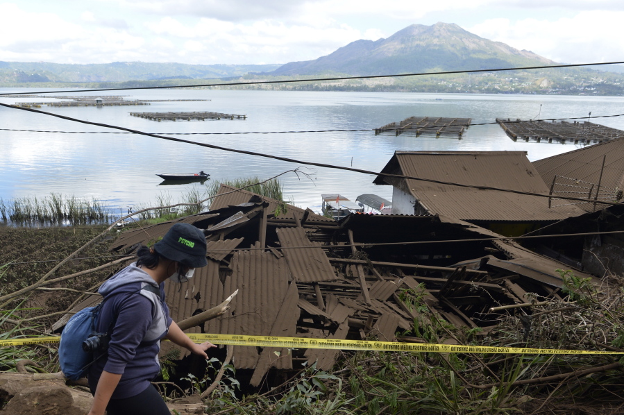 A woman walks past houses by Lake Batur which were damaged by an earthquake-triggered landslide in Bangli, on the island of Bali, Indonesia, Saturday, Oct. 16, 2021. A few people were killed and another several were injured when a moderately strong earthquake and an aftershock hit the island early Saturday.