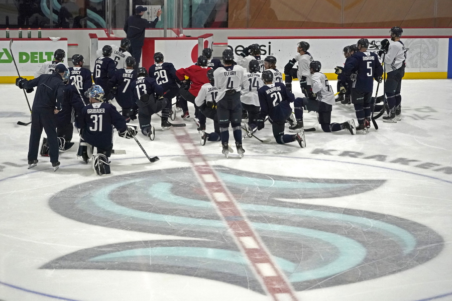 Seattle Kraken players kneel on the ice at their training facility as head coach Dave Hakstol outlines a play during NHL hockey practice, Thursday, Oct. 21, 2021, in Seattle. The Kraken will face the Vancouver Canucks, Saturday in Seattle for the expansion team's home opener. (AP Photo/Ted S.