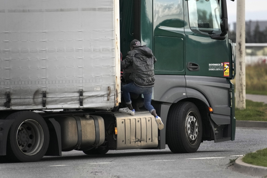 A migrant jumps on a truck in Calais, northern France, Thursday, Oct. 14, 2021, to cross the tunnel heading to Britain.  In a dangerous and potentially deadly practice, he is trying to get through the heavily policed tunnel linking the two countries by hiding on a truck.