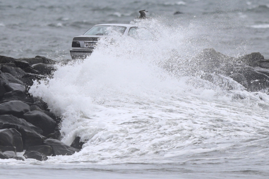 A car making its way across the Gooseberry Island causeway, Tuesday, Oct. 26, 2021, in Westport, Mass., is covered by a large wave, as a nor'easter makes its way across the northeast.