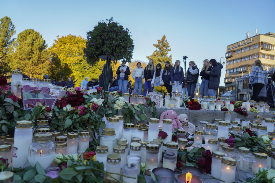 Young people look at the floral tributes and candles left for the victims of a bow and arrow attack, on Stortorvet in Kongsberg, Norway, Friday, Oct. 15, 2021. The suspect in a bow-and-arrow attack that killed five people and wounded three in a small Norwegian town is facing a custody hearing Friday. He won't appear in court because he has has confessed to the killings and has agreed to being held in custody.