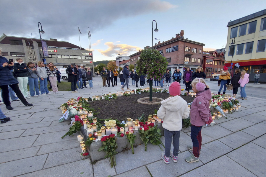 People gather around flowers and candles after a man killed several people on Wednesday afternoon, in Kongsberg, Norway, Thursday, Oct. 14, 2021.