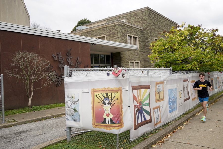 This photo from Oct. 16, 2021, shows the dormant landmark Tree of Life synagogue as a man jogs past the fencing with artwork submitted by Pittsburgh area school students in Pittsburgh's Squirrel Hill neighborhood. Renowned architect Daniel Libeskind is among those working to transform the site to share space with the Holocaust Center of Pittsburgh. The goal to create a solemn memorial as well as a place of regular activity is underway as the date marking the third year since 11 people were killed in America's deadliest antisemitic attack on Oct. 27, 2018 approaches.