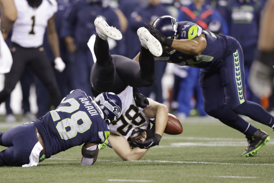 New Orleans Saints' Adam Trautman (82) fumbles between Seattle Seahawks' Ugo Amadi (28) and Bobby Wagner (54) during the second half of an NFL football game, Monday, Oct. 25, 2021, in Seattle. The Seahawks recovered the ball.