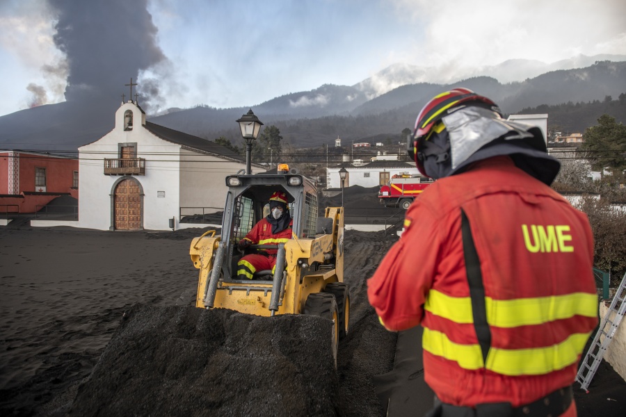 Military Emergency Unit personal clear black ash from volcano as it continues to erupt lava behind a church on the Canary island of La Palma, Spain on Wednesday Oct. 13, 2021. A new lava stream from an erupting volcano threatened to engulf another neighborhood on its way toward the Atlantic Ocean. Island authorities have ordered the evacuation of around 800 people from a section of the coastal town on Tuesday after the lava took a new course and put their homes in its probable path of destruction.