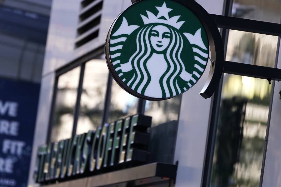 The "Siren" logo hangs outside a Starbucks Coffee shop, Wednesday, July 14, 2021, in Boston. Starbucks said Wednesday, Oct. 27 it is raising its U.S. employees' pay and making other changes to improve working conditions in its stores.