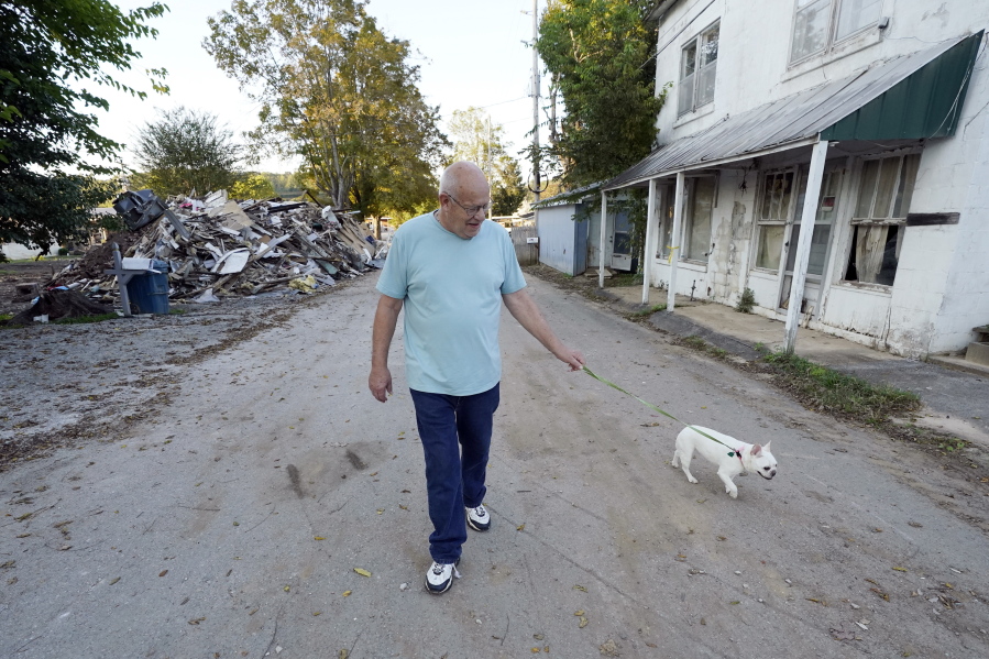 Tommy Goodwin walks his dog, Tasha, down a street lined with flood-damaged buildings and piles of debris Sept. 27, 2021, in Waverly, Tenn. After a devastating flood hit Aug. 21, the town of just over 4,000 people faces a dilemma. More than 500 homes and 50 businesses were damaged. That will likely result in massive revenue losses while the city spends millions on cleanup and repairs. If those homes and businesses don't return, the town could die a lingering death. But if they build back along the creek, they could be risking another disaster.