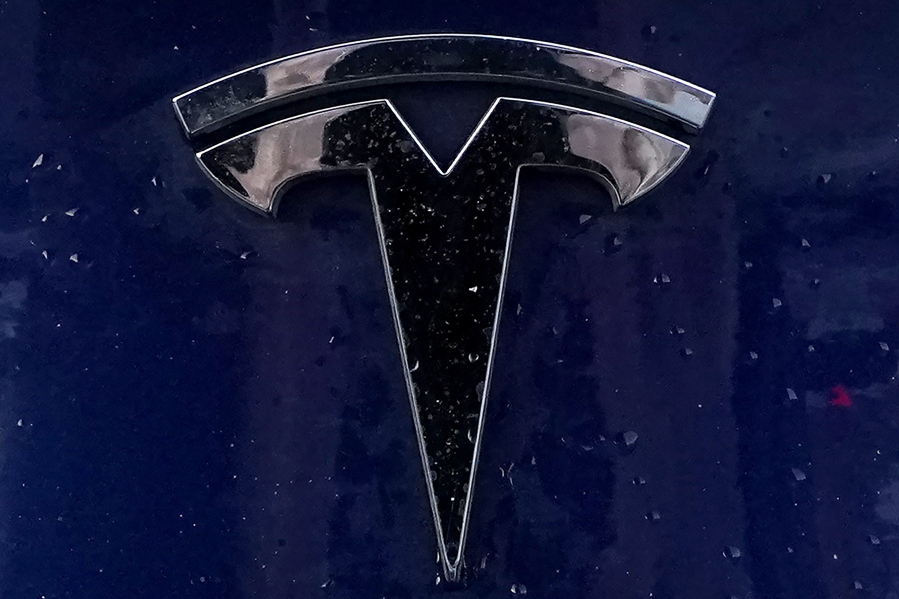 FILE - A Tesla electric vehicle emblem is affixed to a passenger vehicle Sunday, Feb. 21, 2021, in Boston.  U.S. highway safety investigators want to know why Tesla didn't file recall paperwork when it updated Autopilot software so it would do a better job spotting parked emergency vehicles. In a letter sent to Tesla on Tuesday, Oct. 12, the National Highway Traffic Safety Administration told the electric car maker that it has to do a recall if an over-the-internet update mitigates a safety defect.