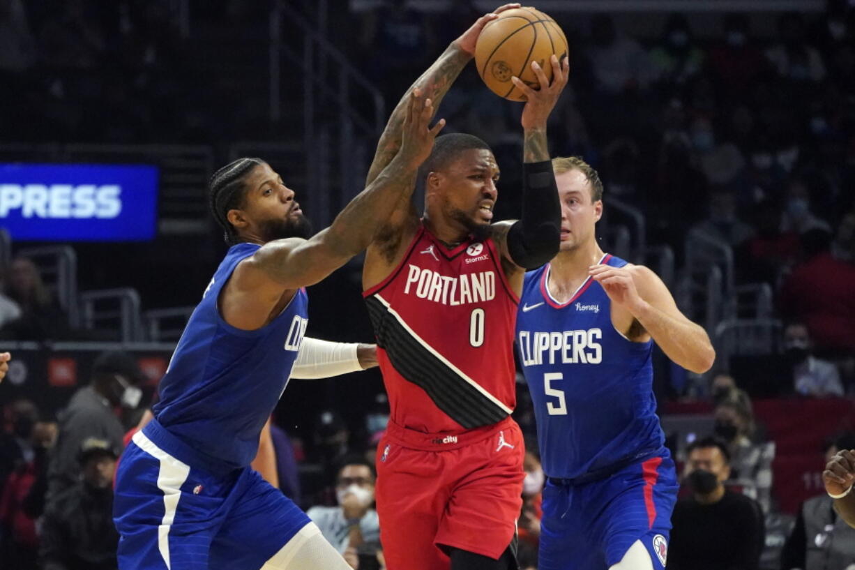 Los Angeles Clippers guard Paul George, left, and guard Luke Kennard (5) defend against Portland Trail Blazers guard Damian Lillard (0) during the first half of an NBA basketball game Monday, Oct. 25, 2021, in Los Angeles.