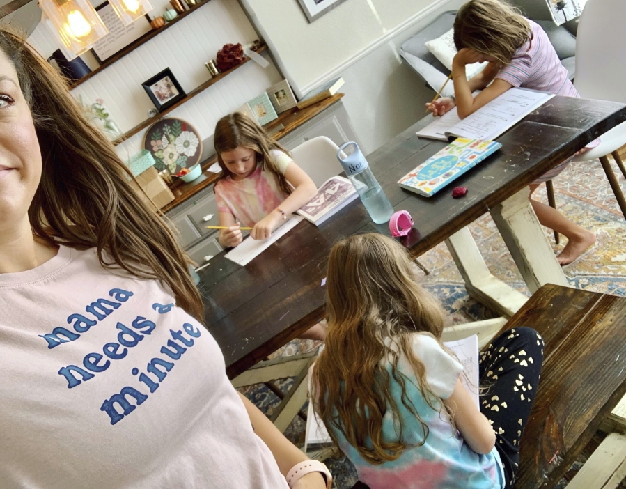 This photo provided by Amber Cessac shows Amber Cessac taking a selfie as her daughters do their homework at their home in Georgetown, Texas on Sept. 9, 2021. A year and a half in, the pandemic is still agonizing families. There is still the exhaustion of worrying about exposure to COVID-19 itself, and the policies at schools and day cares where children spend their time. The spread of the more infectious delta variant, particularly among people who refuse vaccinations, has caused a big increase in infections in children. But there's also COVID exposures and illnesses -- and even minor colds -- at schools and day cares that mean children get sent home, forcing parents to scramble for child care.
