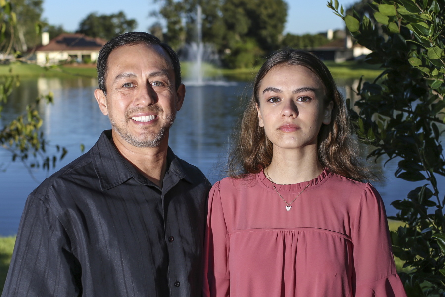 Portrait of Mitch Arbelaez and his daughter Jayden in Jacksonville, Fla., Wednesday, Oct. 13, 2021.  Banned from the Florida hospital room where her mother lay dying of COVID-19, Jayden Arbelaez pitched an idea to construction employees working nearby.  The workers gave the 17-year-old a yellow vest, boots, a helmet and a ladder to climb onto a section of roof so she could look through the window and see her mother, Michelle Arbelaez, alive one last time.