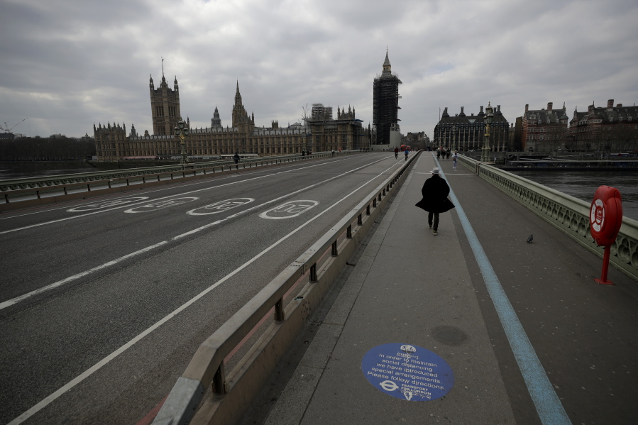 FILE - In this Tuesday, March 23, 2021 file photo, people pass over a quiet Westminster Bridge, backdropped by the scaffolded Houses of Parliament and the Elizabeth Tower, known as Big Ben, in London, during England's third coronavirus lockdown. The British government waited too long to impose a lockdown in the early days of the COVID-19 pandemic, missing a chance to contain the disease and leading to thousands of unnecessary deaths, lawmakers concluded Tuesday, Oct. 12, 2021 in a hard-hitting report.