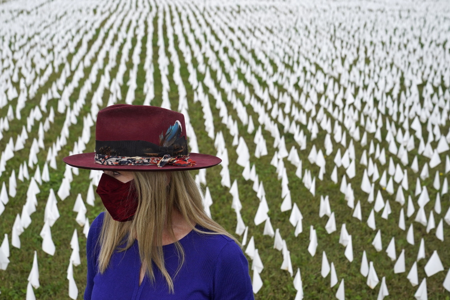 FILE - In this Oct. 27, 2020, file photo, Artist Suzanne Brennan Firstenberg stands among thousands of white flags planted in remembrance of Americans who have died of COVID-19, near Robert F. Kennedy Memorial Stadium in Washington. Firstenberg's temporary art installation, called "In America, How Could This Happen," will include an estimated 240,000 flags when completed.
