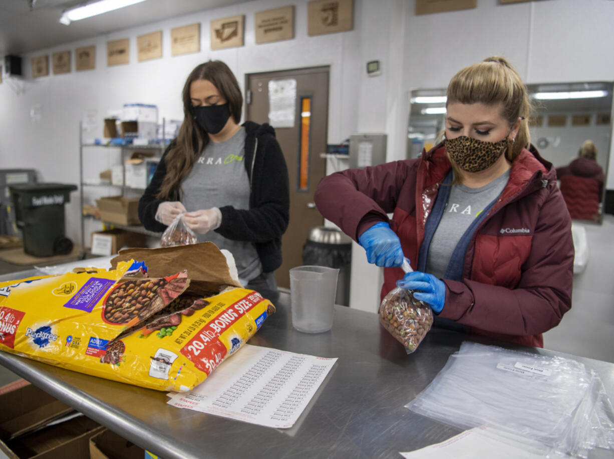 Portland residents Sarah Vernarecci, left, and Rachel Russo, right, tie bags of dog food during a volunteer shift at the Clark County Food Bank.