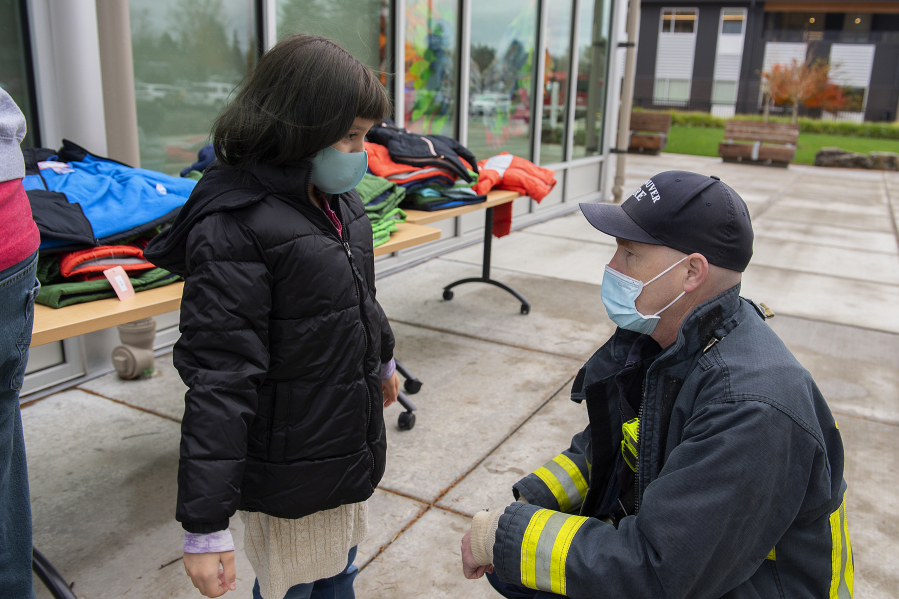 Fourth-grader Maria Bella, left, tries on warm winter coats with the help of Capt. Marc Patchin at Marshall Elementary School on Friday morning. The Vancouver Firefighters Union (I.A.F.F. Local 452) in cooperation with the City of Vancouver Fire Department, private donors and local businesses donated coats to local children.