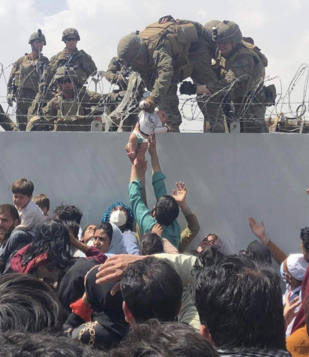 This image made available to AFP on Aug. 20, 2021 by Human Rights Activist Omar Haidari, shows a U.S. Marine grabbing an infant over a fence of barbed wire during an evacuation at Hamid Karzai International Airport in Kabul on Aug. 19, 2021.