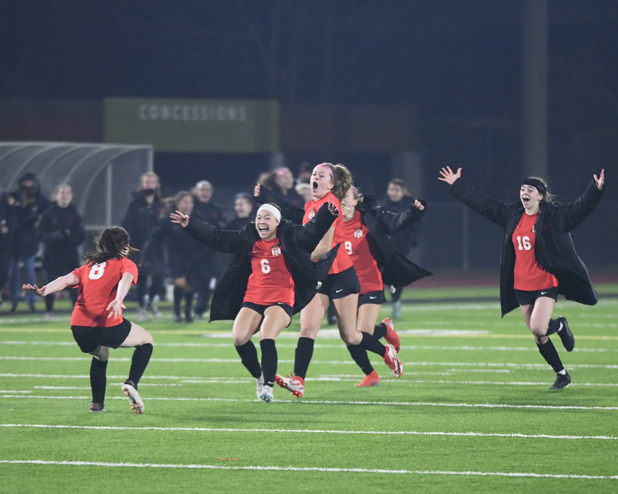 Camas girls soccer team members Jasmine Whittington (6), Anna Mooney and Lily Loughney (16) charge in celebration toward Nora Melcher (8) after Melcher converted the winning goal in the penalty-kick shootout in the Papermakers? win over Issaquah for the 4A state championship in Puyallup on Nov. 20, 2021.