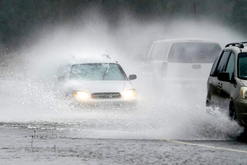 A westbound car is caught in a spray of water thrown up by a pickup truck on Highway 20 Monday, Nov. 15, 2021, near Hamilton, Wash. The heavy rainfall of recent days will brought major flooding of the Skagit River that is expected to continue into at least Monday evening.