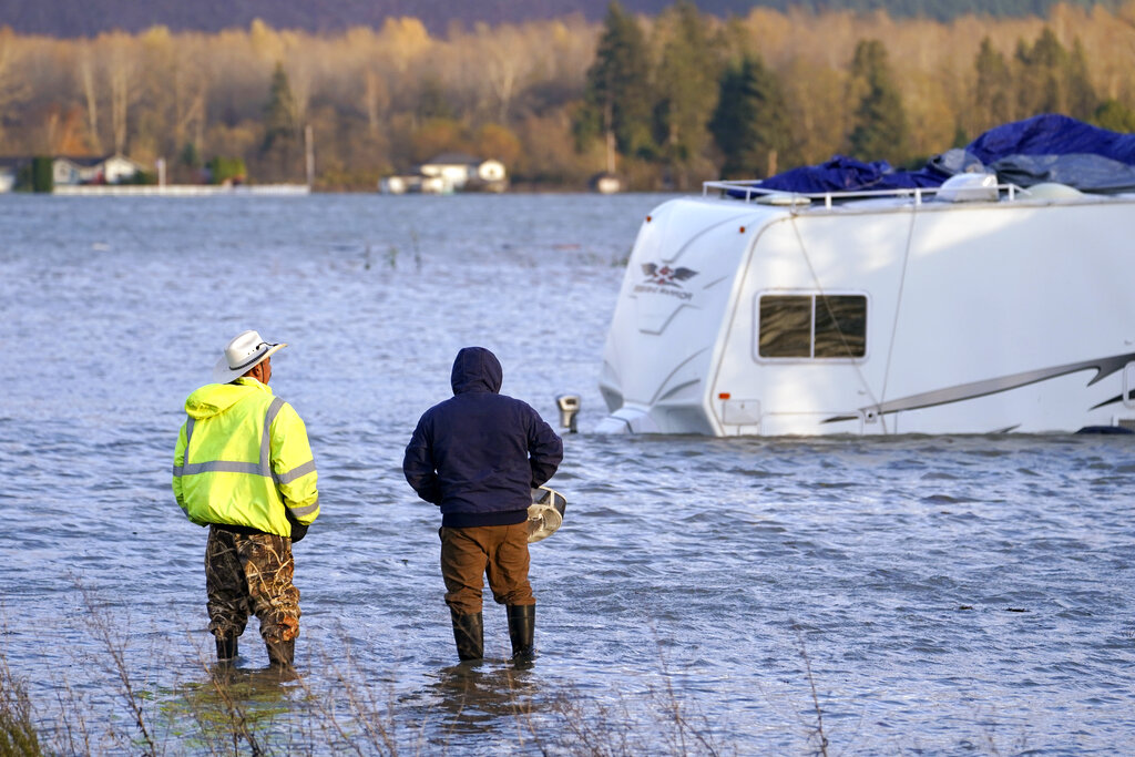 Two men stand in the flooded Skagit River and look across at an RV, Monday, Nov. 15, 2021, in Sedro-Woolley, Wash.