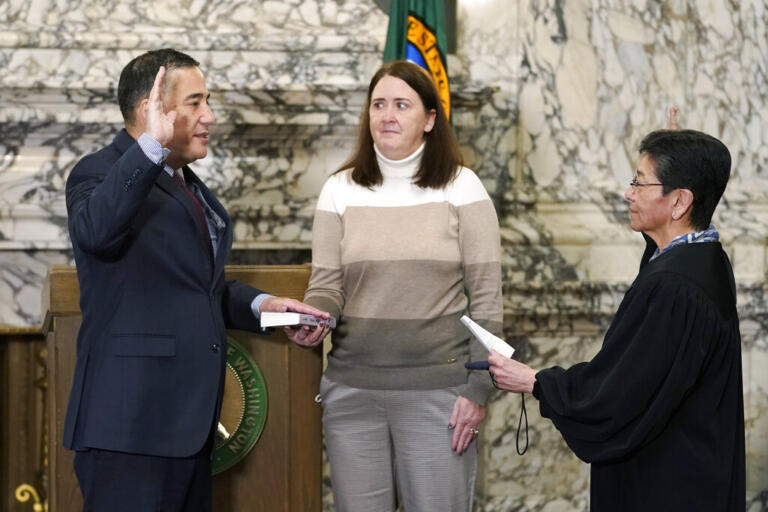 Steve Hobbs, left, is sworn by state Supreme Court Justice Mary Yu, right, as Washington Secretary of State, Monday, Nov. 22, 2021, at the Capitol in Olympia, Wash., as his wife Pam, center, looks on. Hobbs, a former state senator from Lake Stevens, Wash., is the first person of color to head the office and the first Democrat to serve as secretary in more than 50 years. He replaces Republican Secretary of State Kim Wyman, who resigned to accept an election security job in the Biden administration. (AP Photo/Ted S.