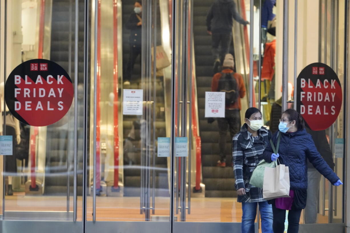 FILE - Black Friday shoppers wear face masks and gloves during the coronavirus pandemic as they leave the Uniqlo store along Fifth Avenue, Friday, Nov. 27, 2020, in New York. Retailers are expected to usher in the unofficial start to the holiday shopping season Friday, Nov. 26, 2021, with bigger crowds than last year in a closer step toward normalcy. But the fallout from the pandemic continues to weigh on businesses and shoppers' minds.