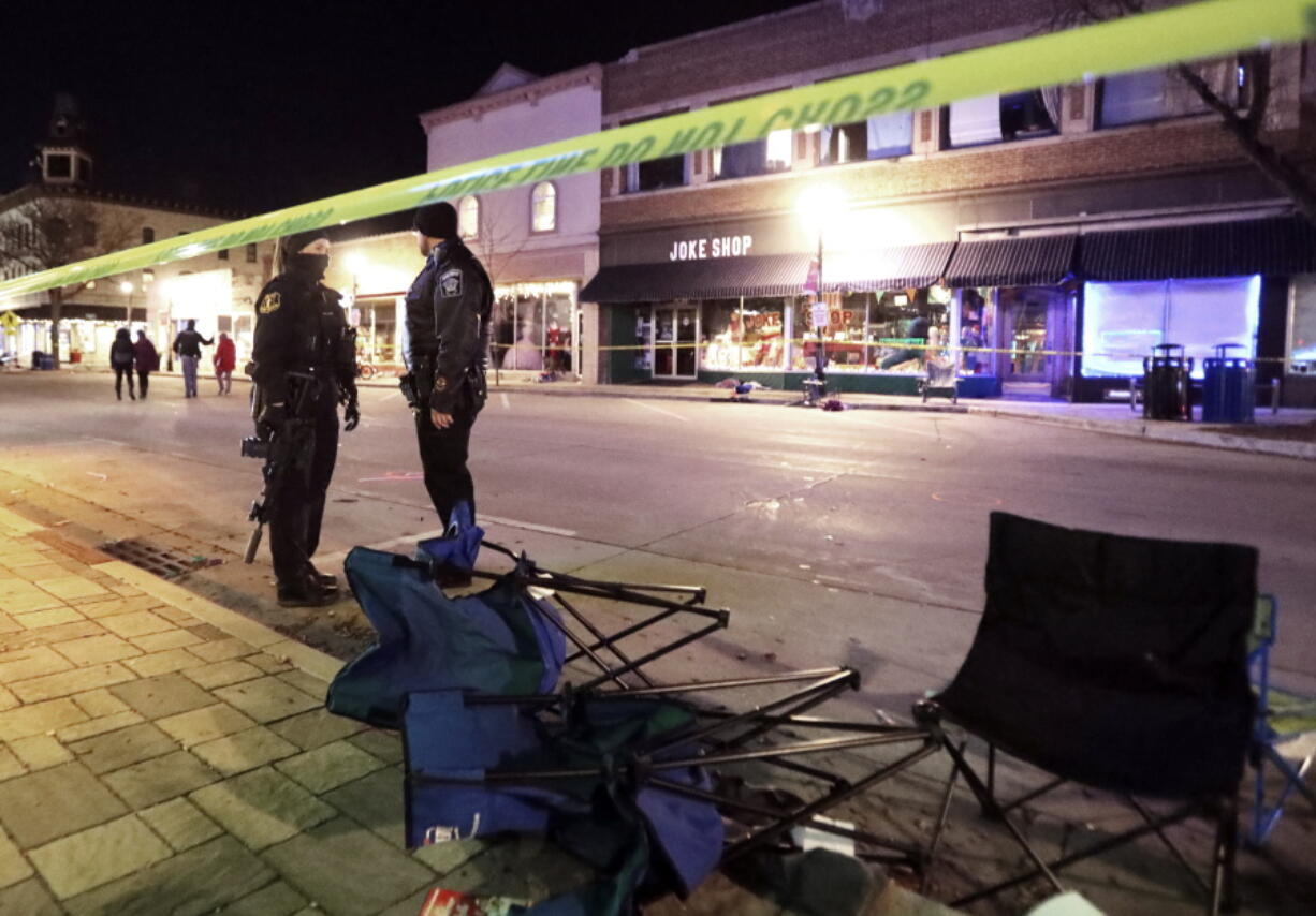 Police stand near toppled chairs lining W. Main St. in downtown Waukesha, Wis.,  after an SUV drove into a parade of Christmas marchers, Sunday, Nov. 21, 2021.
