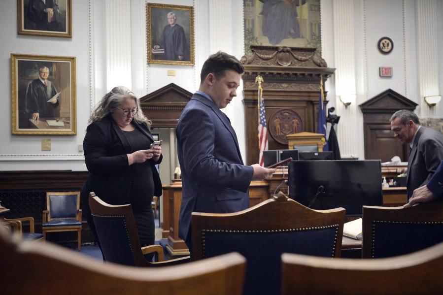 Defendant Kyle Rittenhouse checks his cell phone as he waits with his attorneys for the judge to relieve the jury during his trial at the Kenosha County Courthouse in Kenosha, Wis., on Thursday, Nov. 18, 2021.