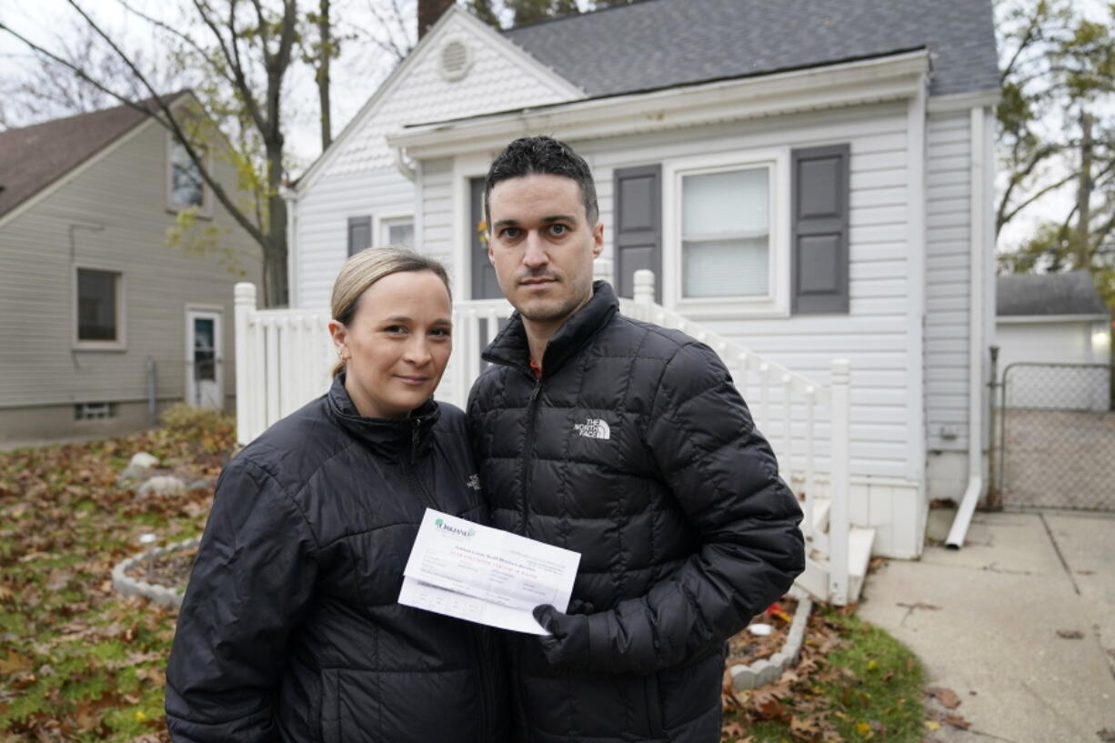 Nicole and Simon Obarto, holding a lead and copper analysis of water from the Oakland County Health Division, stand outside their home in Royal Oak, Mich., on  Thursday, Nov. 18, 2021. The couple had their water line tested for lead and the results were high enough to have the lead service line replaced.