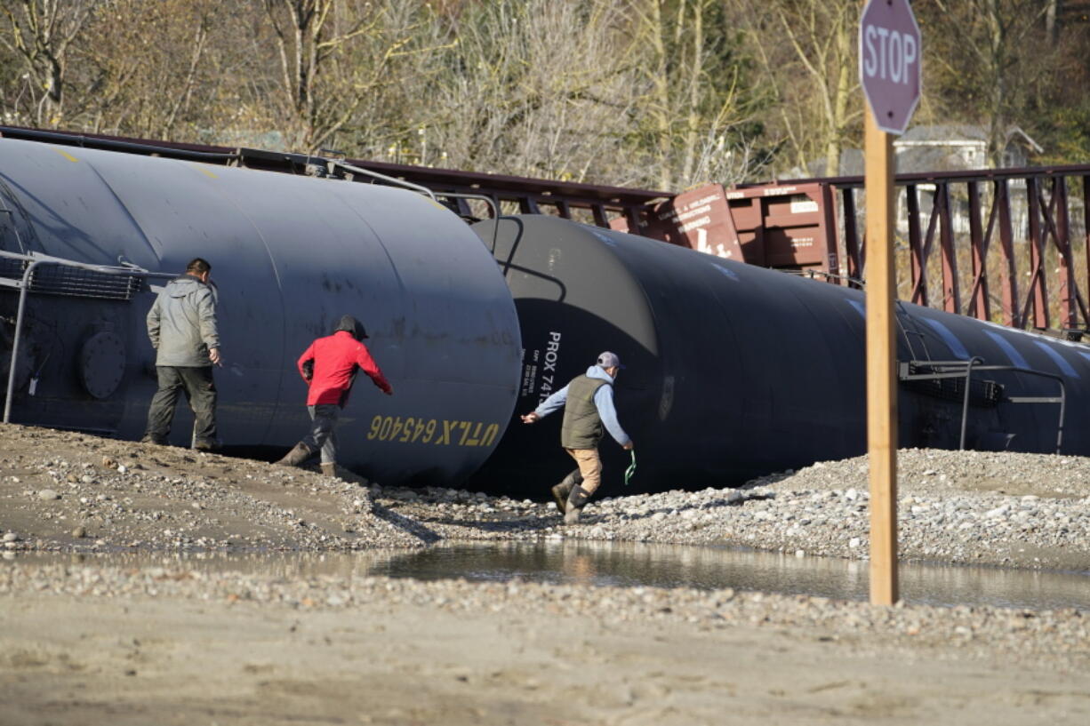 People walk by railroad cars derailed by flooding near tracks at a BNSF rail yard Wednesday, Nov. 17, 2021, in Sumas, Wash. People in the small city of Sumas, Washington, are assessing damage from flooding that hit an estimated three quarters of homes in the community near the Canadian border.