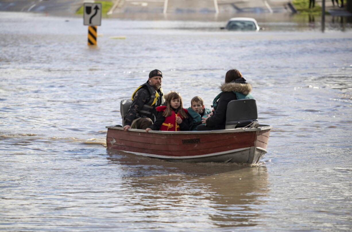A woman and children who were stranded by high water due to flooding are rescued by a volunteer operating a boat in Abbotsford, British Columbia on Tuesday, Nov. 16, 2021. Officials in a small city near the Canada border are calling the damage devastating after a storm that dumped rain for days caused flooding and mudslides. City officials in Sumas, Washington said Tuesday that hundreds of people had been evacuated and estimated that 75% of homes had water damage. Just over the border, residents in about 1,100 rural homes in Abbotsford were told to evacuate as waterways started to rise quickly.